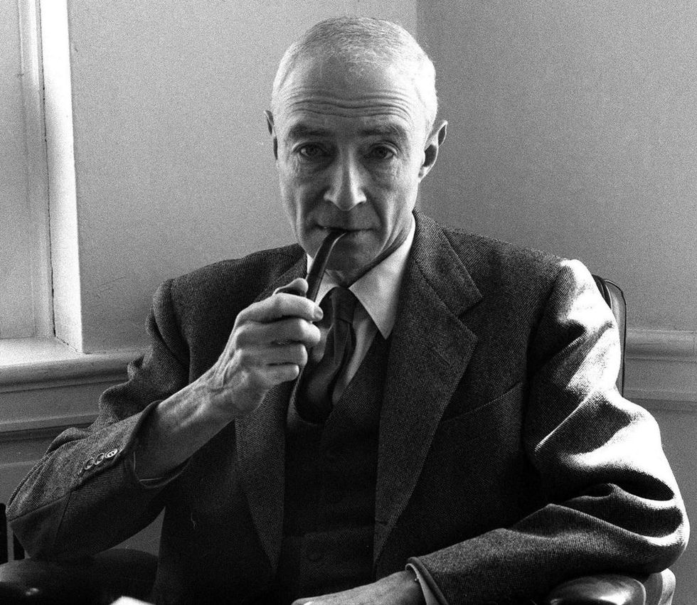j Robert Oppenheimer poarta costum si cravata si tine o pipa in gura